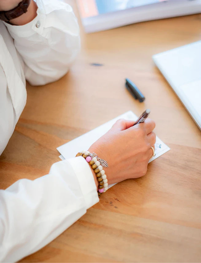 Person schreibt Notizen am Tisch, Fokus auf Hand und Stift.