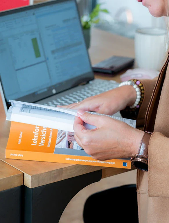 Frau liest Finanzbuch vor einem Laptop bei der Buchhaltungsberatung.